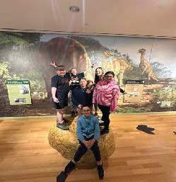 Members of the sixth grade in front of dinosaur wall painting